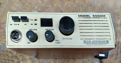 VHF-FM unit with round channel selector, 2 other knobs, 2 push buttons, speaker and a microphone behind on right side